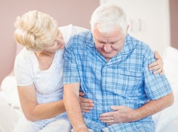 Foto von älterem Mann mit Bauchschmerzen und Frau auf Bettkante