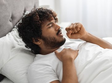 Junger Mann mit Husten im Bett