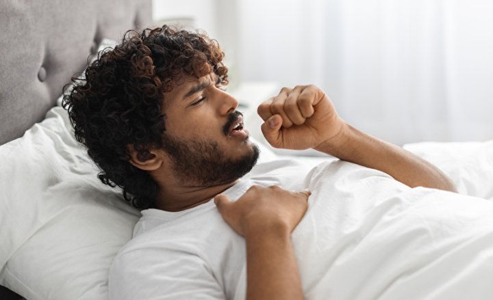 Hustender junger Mann im Bett